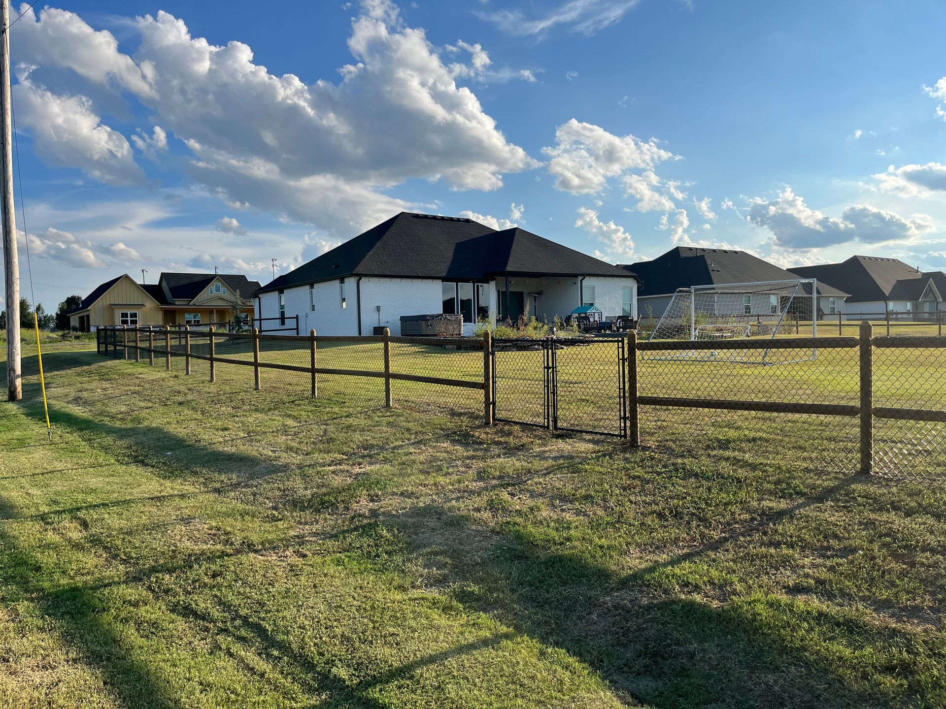 A wooden fence surrounds a grassy field with a house in the background.