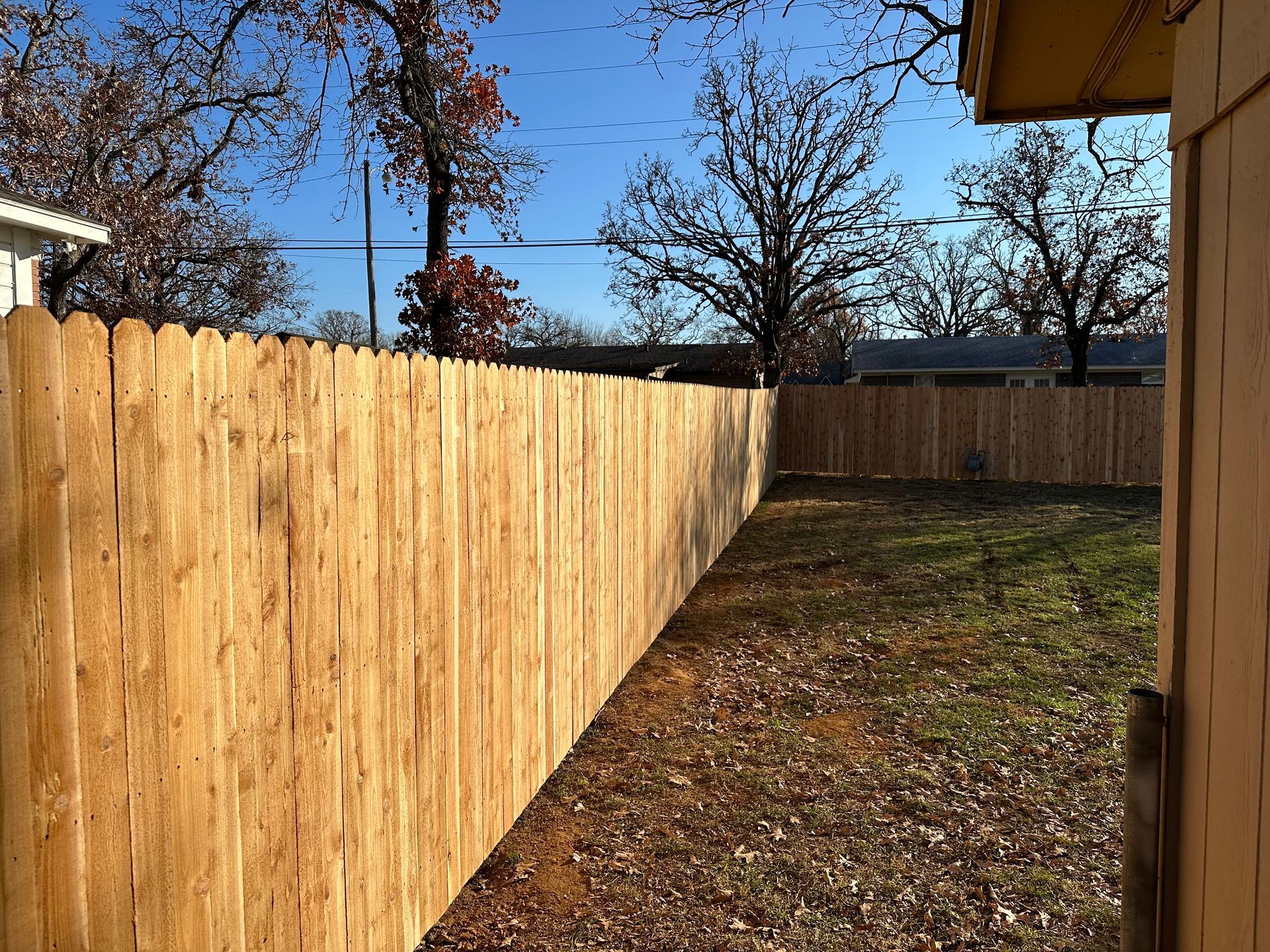 A wooden fence surrounds a backyard with trees in the background.