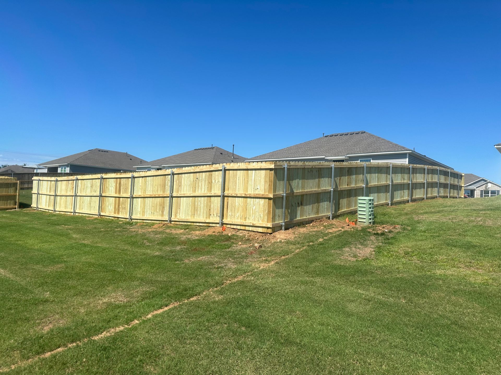 A wooden fence is sitting in the middle of a grassy field in front of a house.