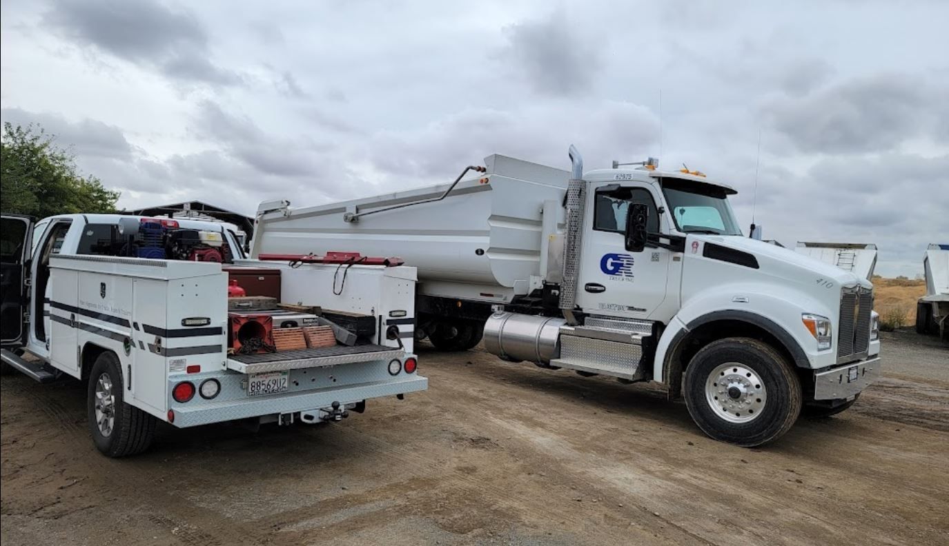 Two white trucks are parked next to each other in a dirt lot.
