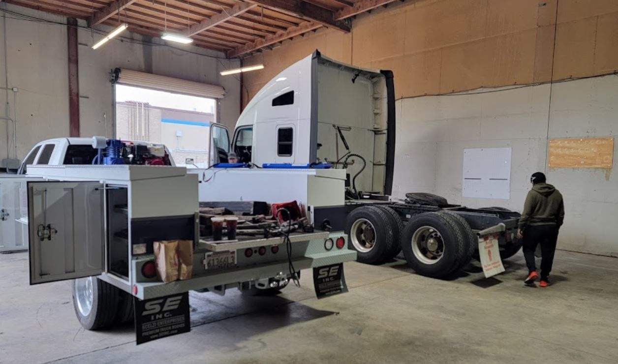 A man is standing next to a semi truck in a garage.