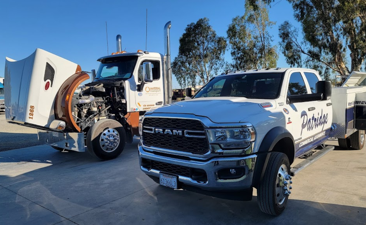 A ram truck is parked next to a semi truck with its hood open.