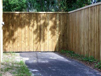 A wooden fence surrounds a driveway with trees in the background.