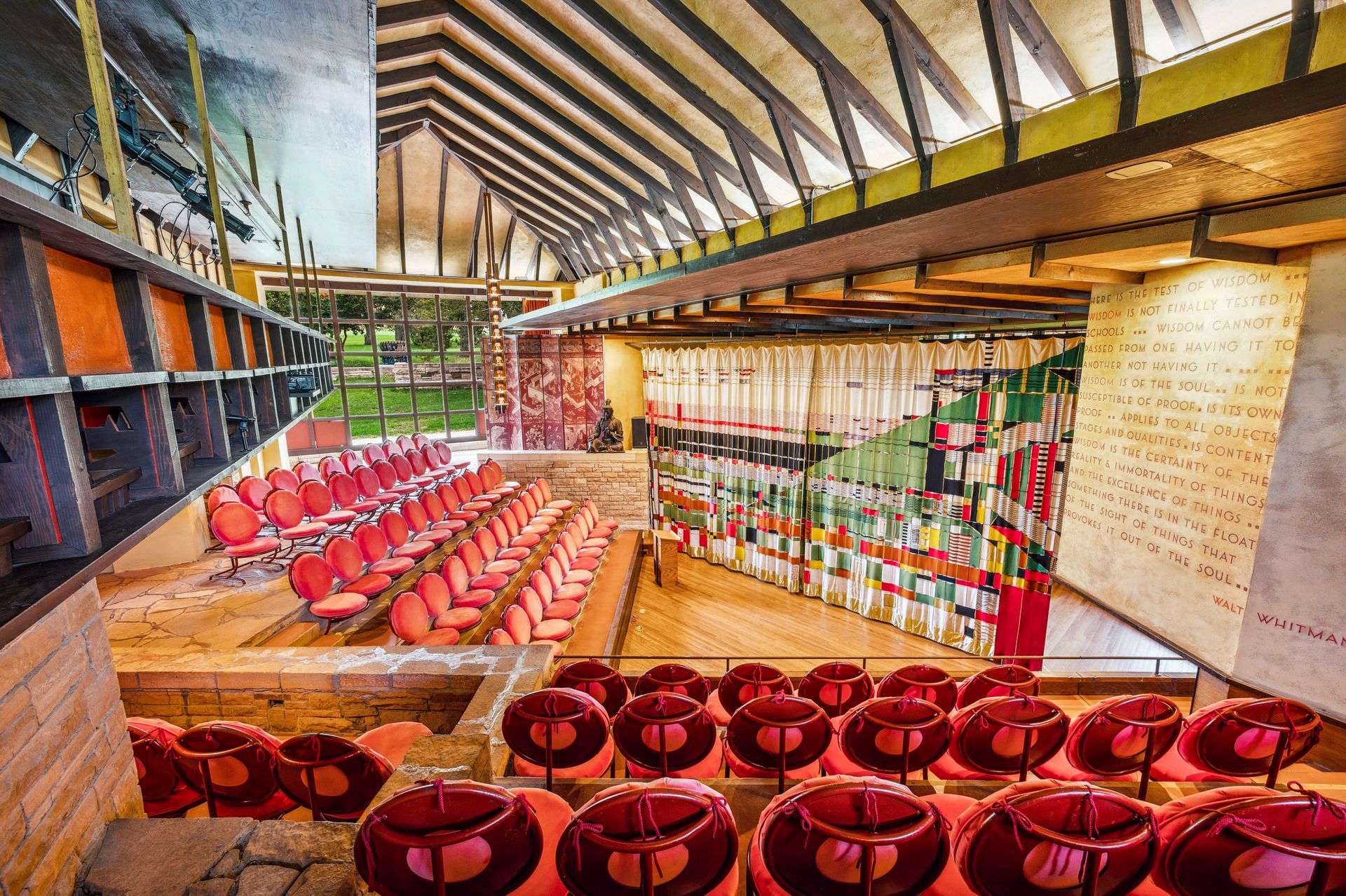 Auditorium interior with red chairs, wood beams, and colorful glass wall.