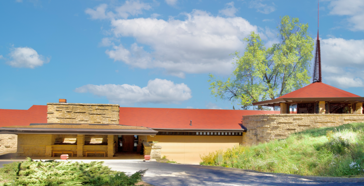 Low-angle view of a brick and stone building with a red roof against a blue sky with fluffy clouds.