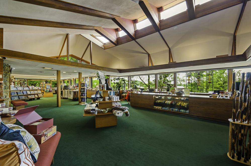 Interior of a store with high ceilings, skylights, and a green carpet. Merchandise is displayed on shelves and tables.
