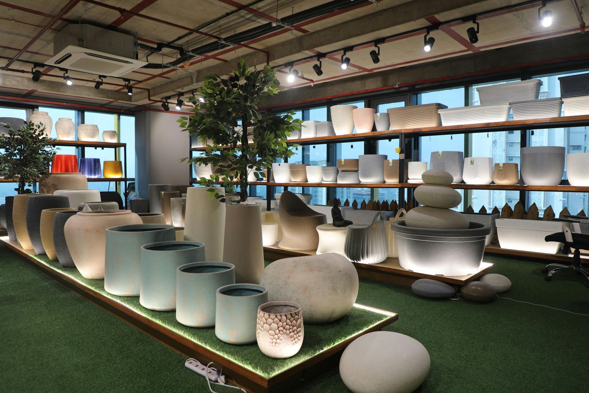 A showroom displaying various minimalist, glowing white and neutral-toned planters and stone-like decor on green carpeting.