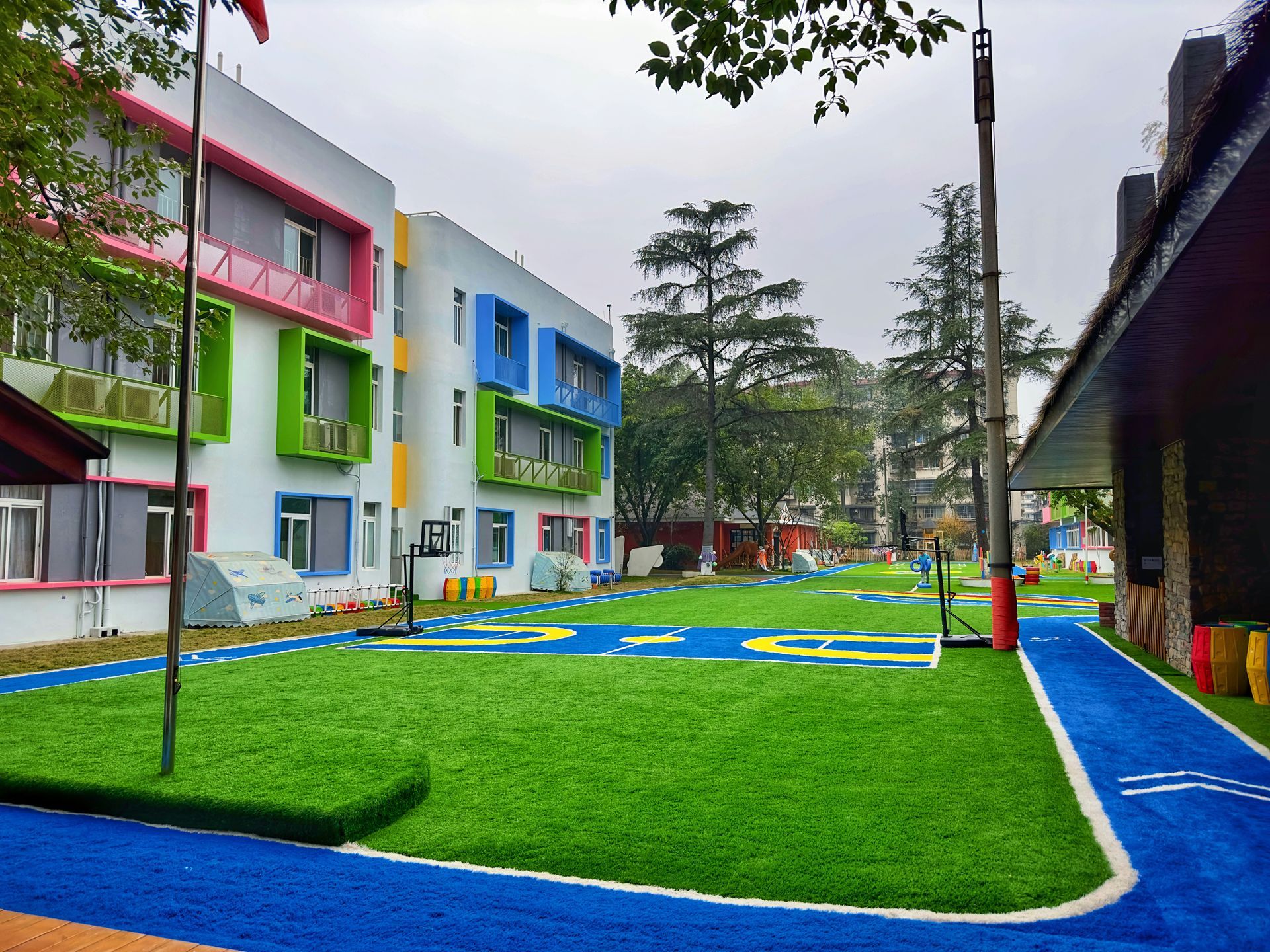 A colorful school building with vibrant green, blue, and pink accents overlooks a bright green lawn and a blue track.