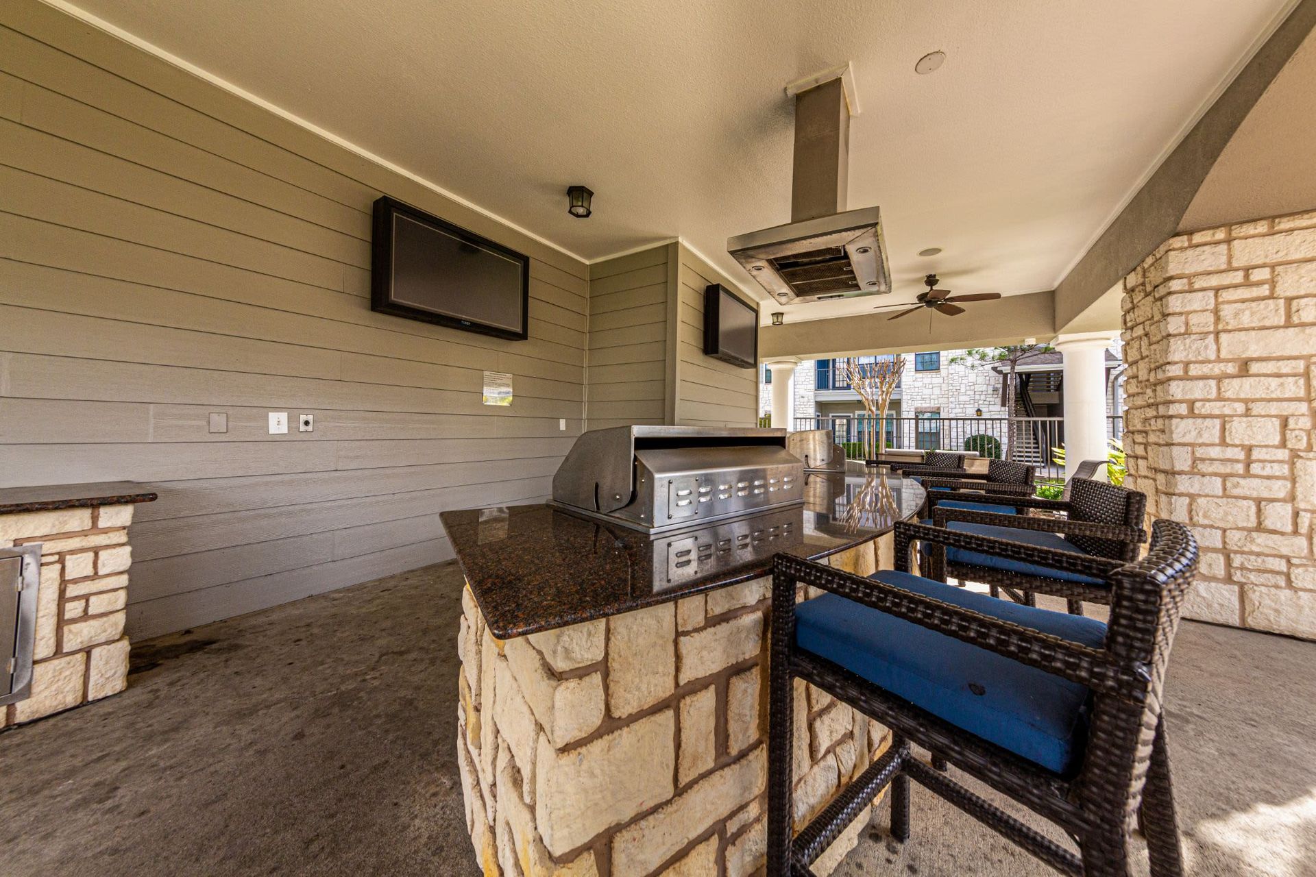 A patio area with a grill, chairs, tables, and televisions at Marquis Grand Lakes in Richmond, TX.