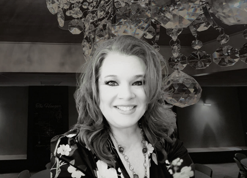 Smiling woman indoors beneath hanging crystal decor, in black-and-white.