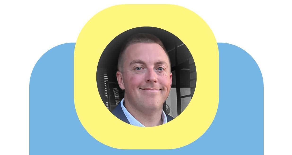 Portrait photo in a yellow circle over a blue rounded background, showing a smiling man outdoors