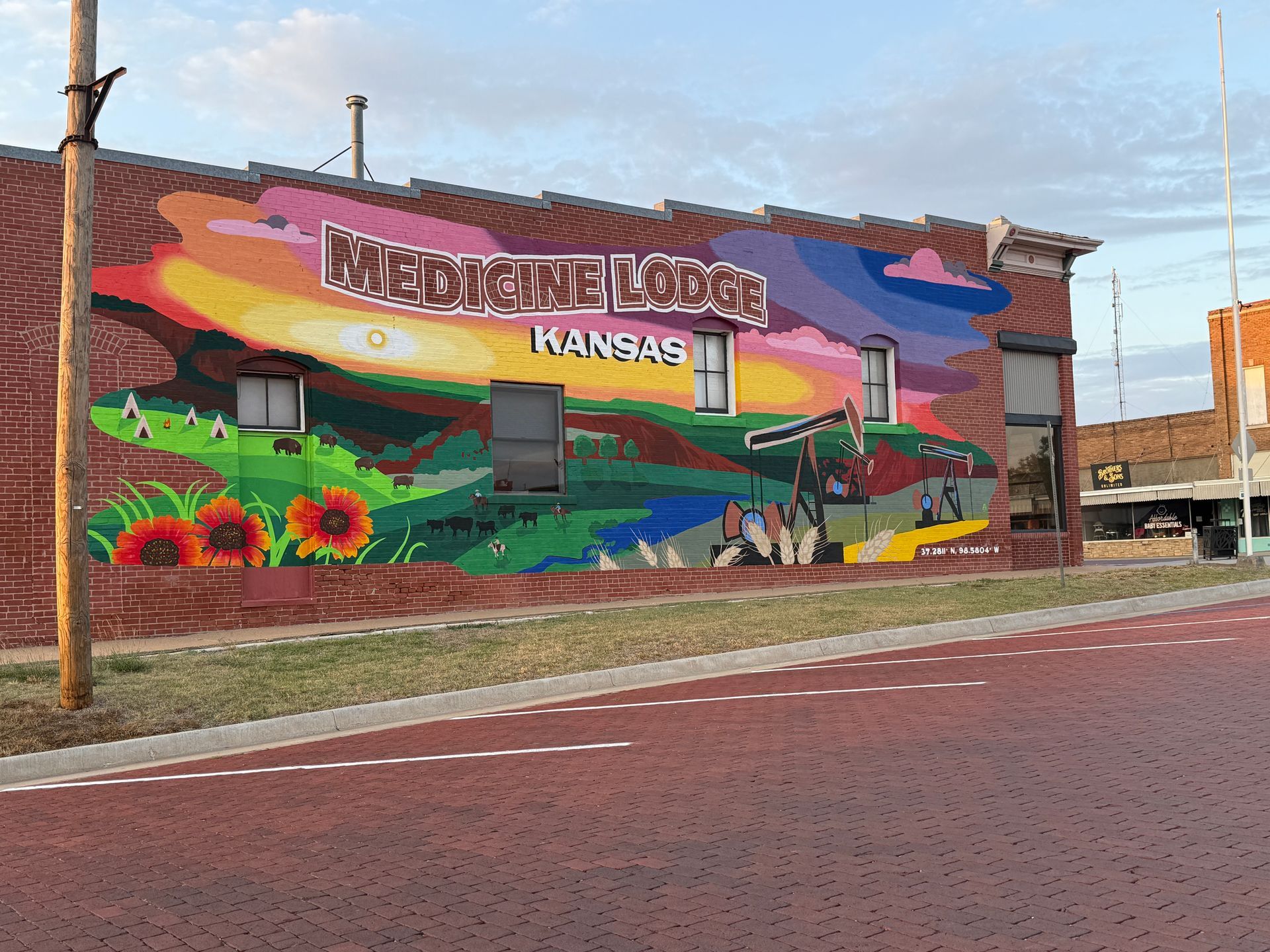 Colorful mural on a brick wall reading “Norton, Kansas,” beside a red street and sidewalk.