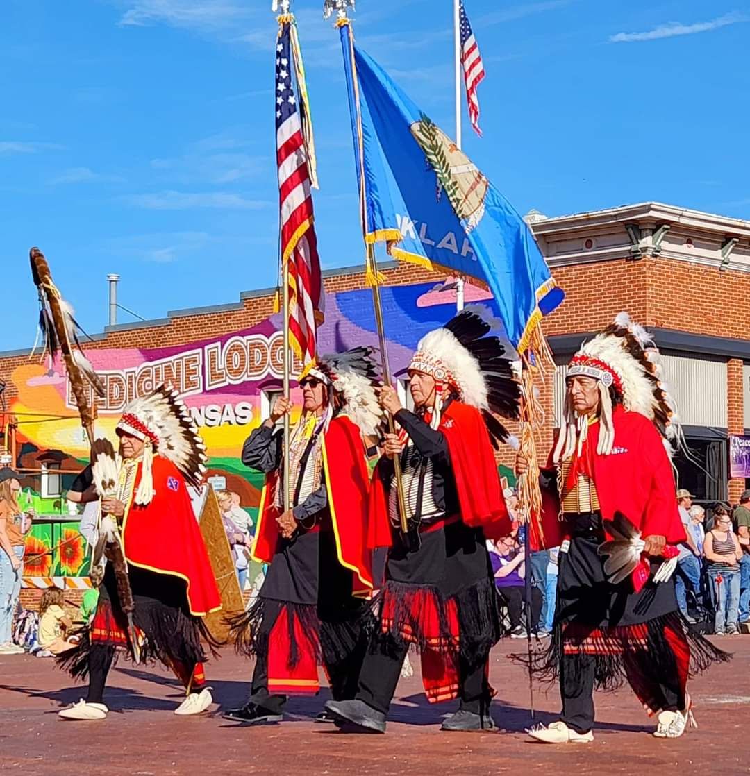 Dancers in red and black attire perform in a street parade carrying flags under a blue sky.