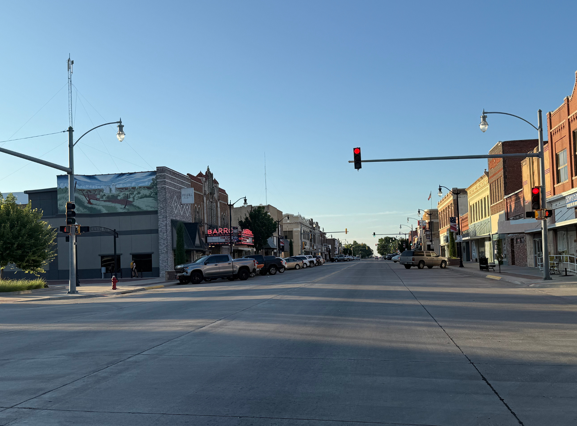 Empty downtown street at a red light with storefronts and a clear blue sky
