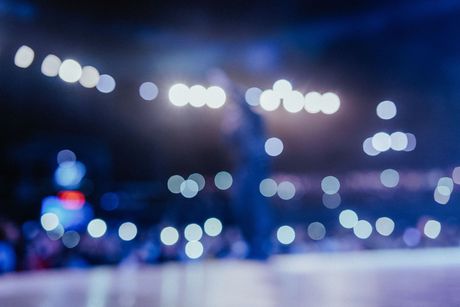 Blurred concert stage with bright blue and white lights and indistinct performers in the background
