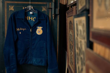Blue embroidered blazer hanging in a narrow hallway, with framed pictures on the wall