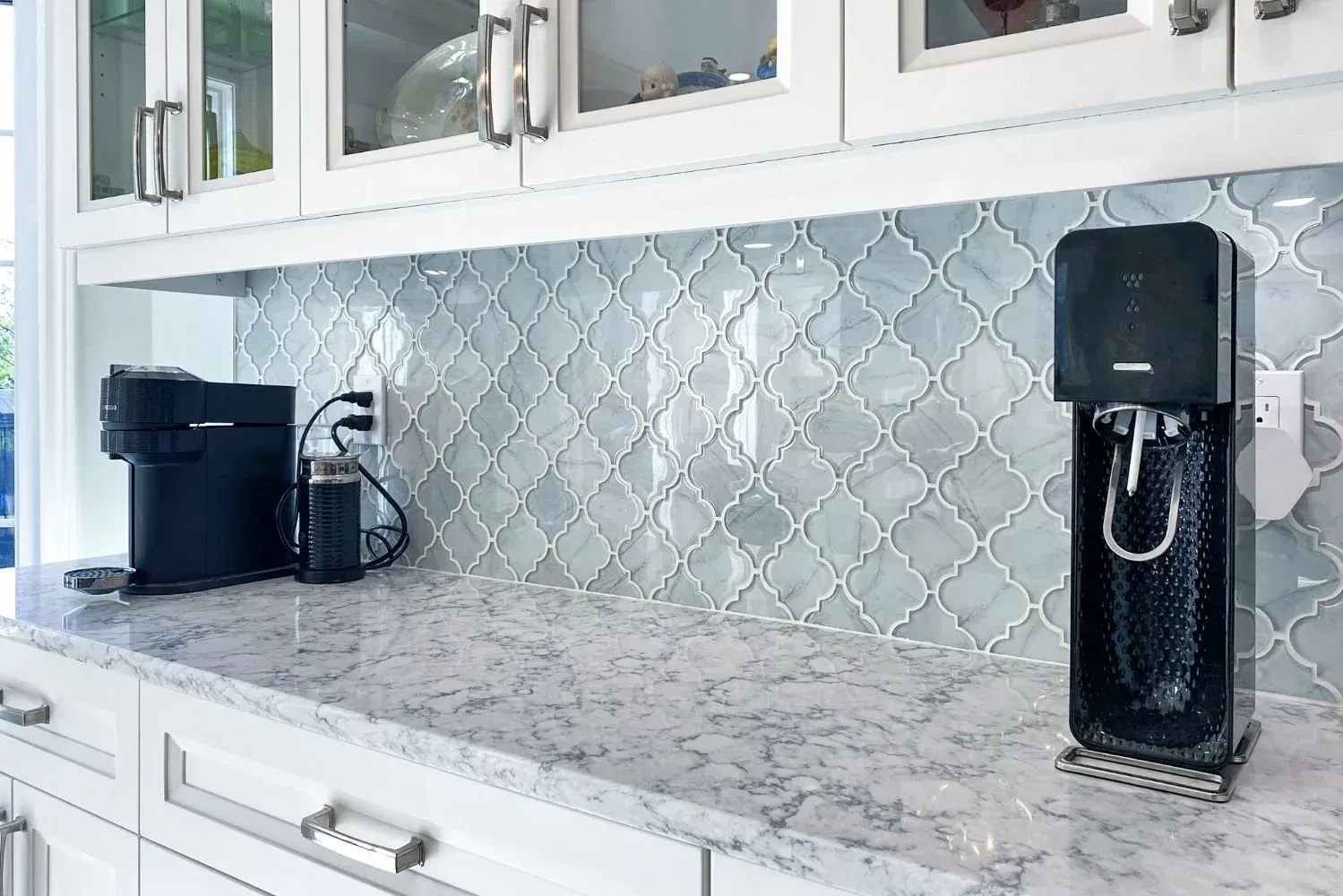 Kitchen countertop with coffee maker, soda maker, and blue-gray tile backsplash.