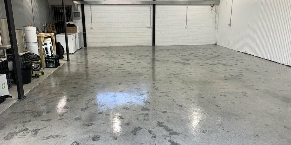 An empty room with a polished concrete floor, white walls, and a closed garage door.