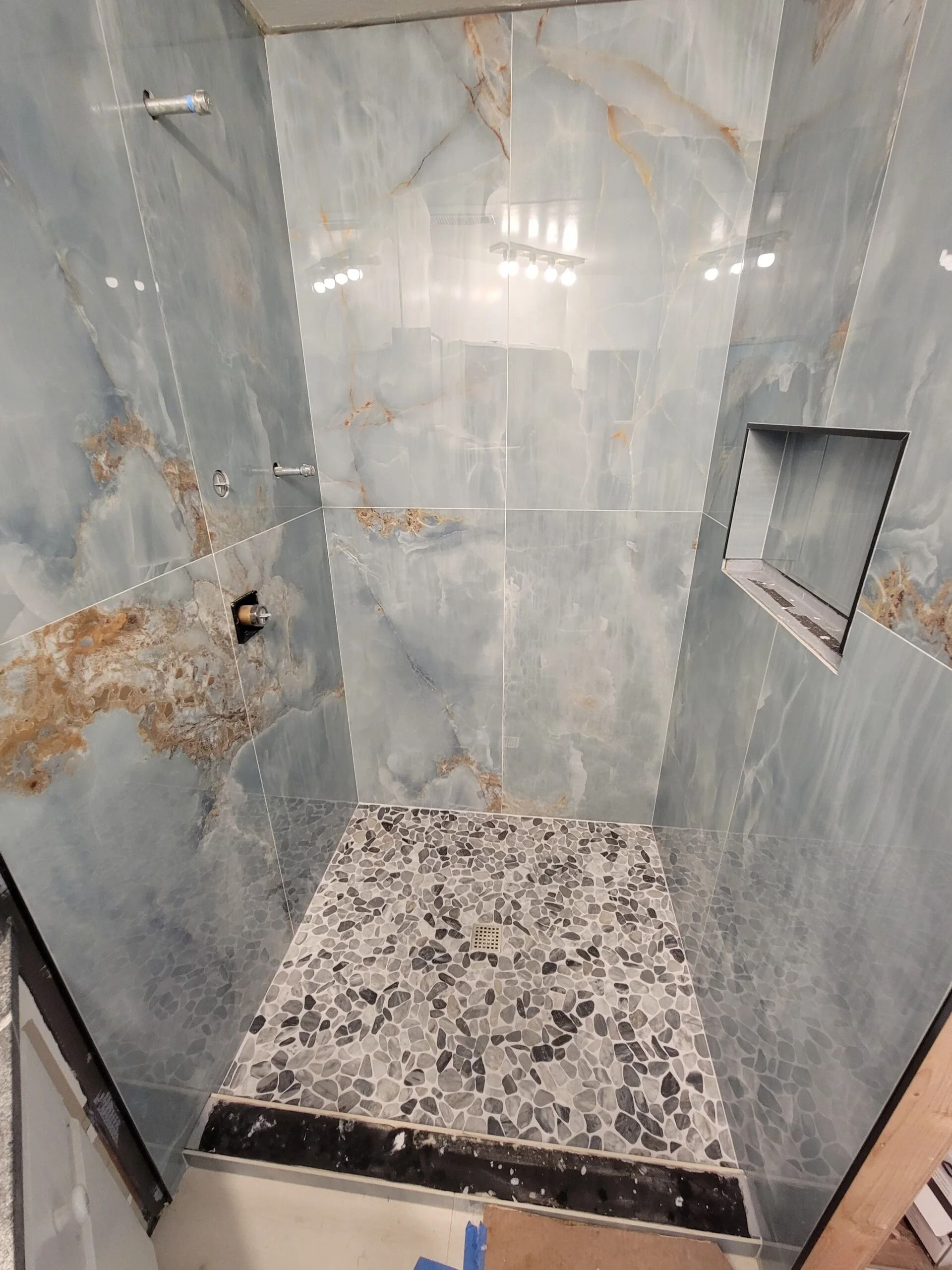 Blue tiled shower with mosaic floor, built-in shelf, and black drain.