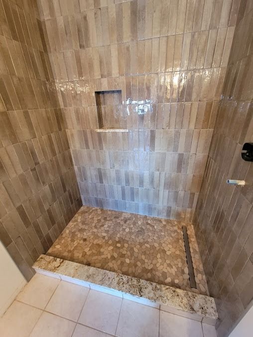 Shower stall with brown tiled walls and a stone pebble floor, featuring a built-in shelf.