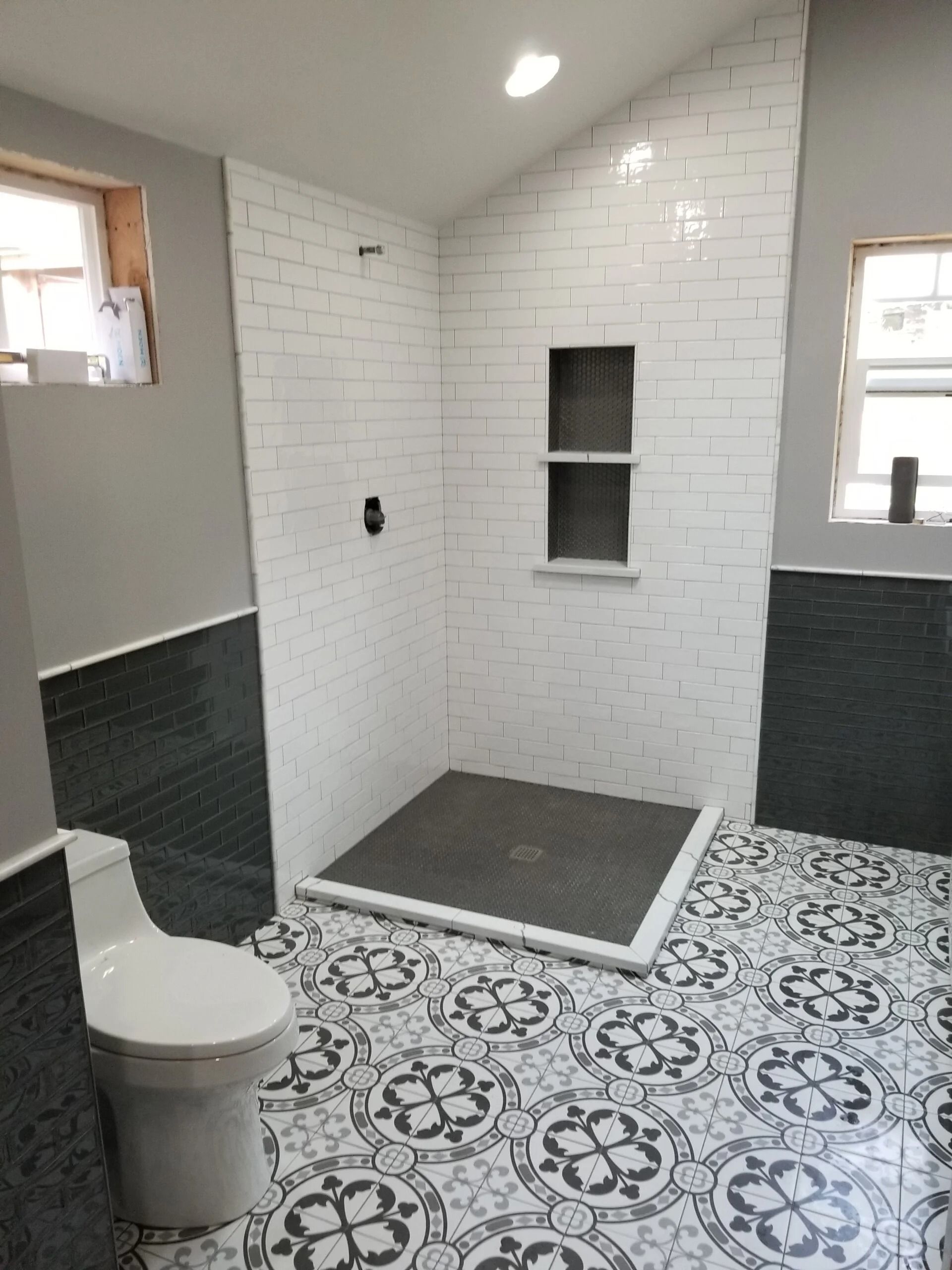 Bathroom with white tiled shower, patterned floor, and a toilet.