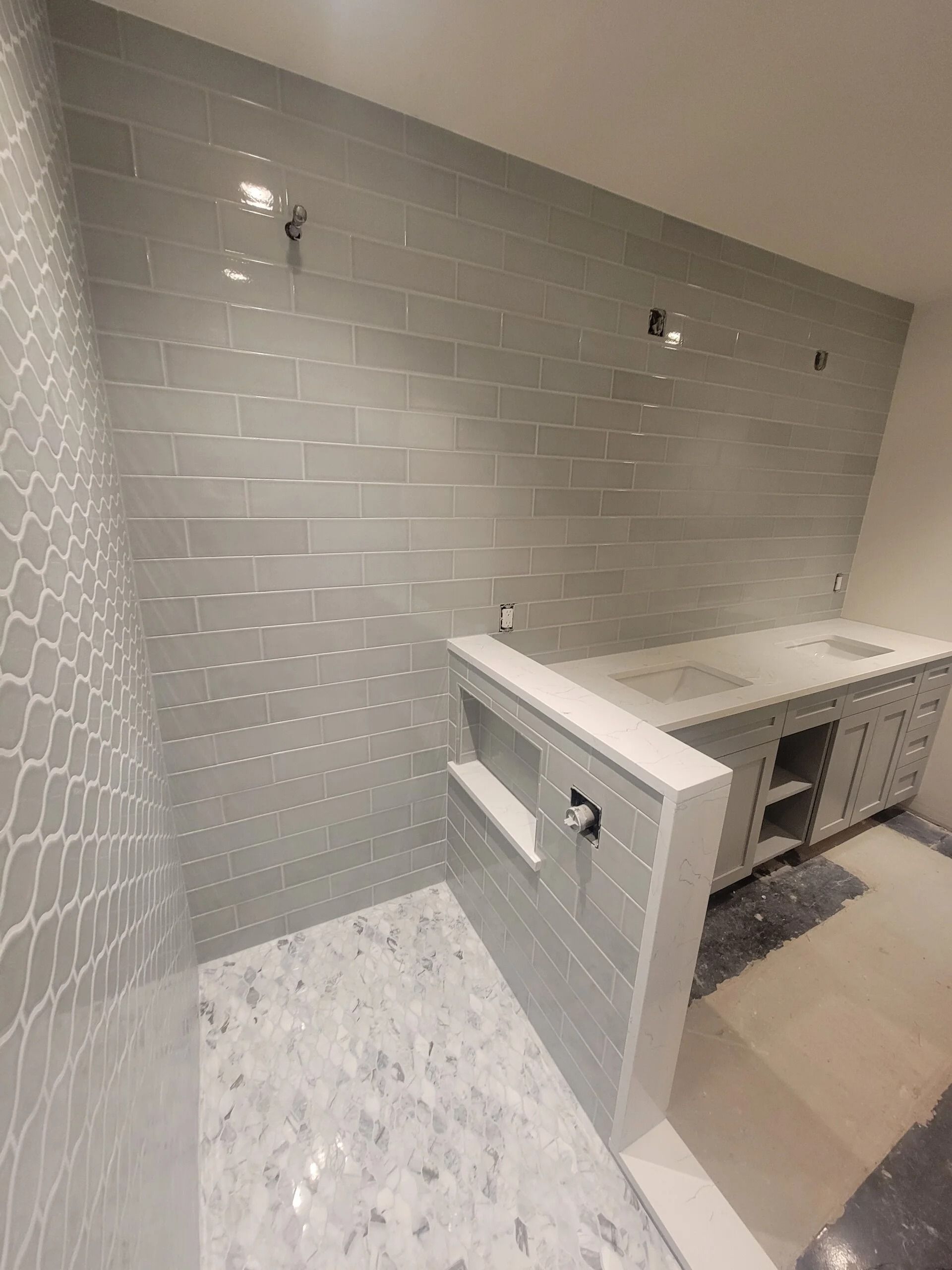 Bathroom with gray tile walls, mosaic shower floor, and a vanity under construction.