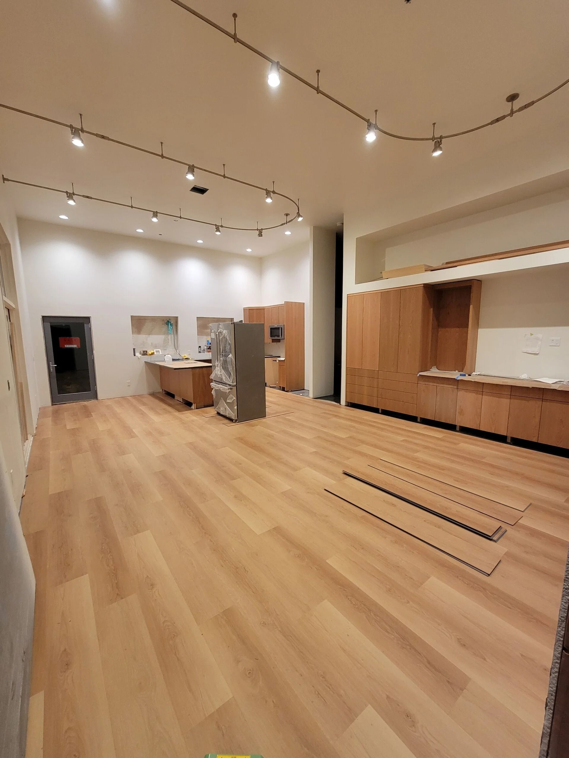 Empty commercial space with wood floors, cabinets, and track lighting.