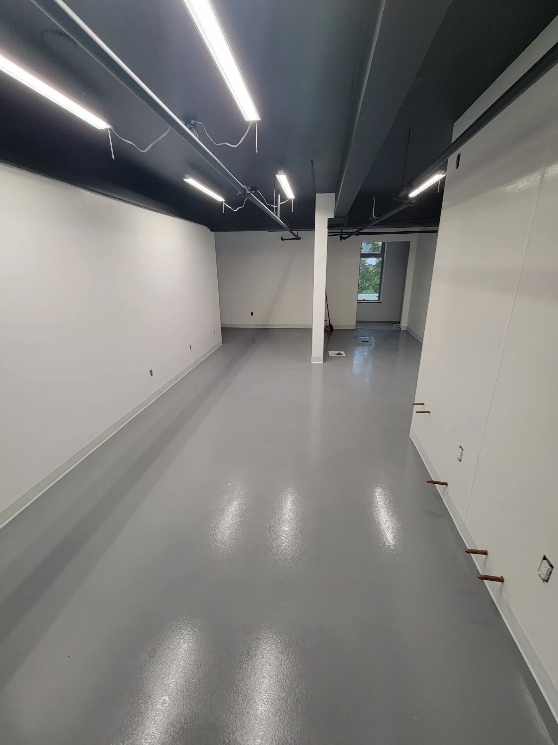 Empty room with gray floor, white walls, and a black ceiling with lights.