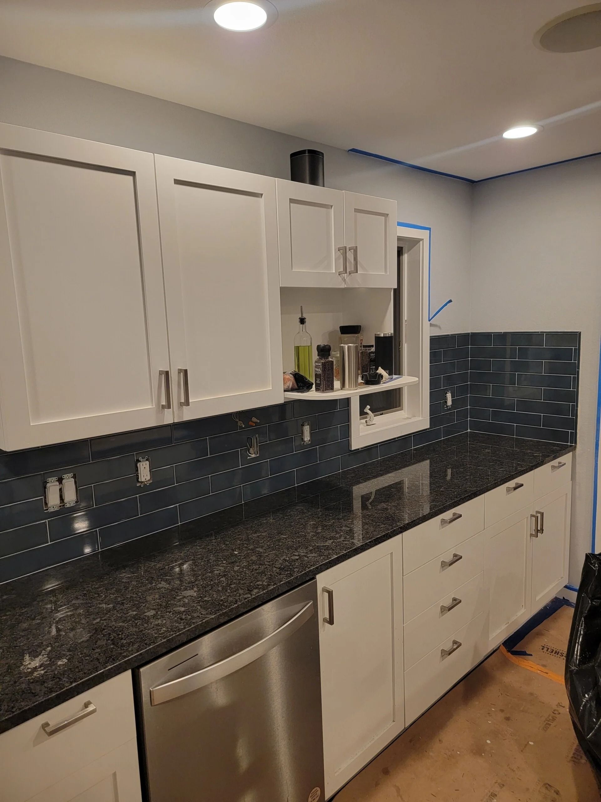 White kitchen cabinets with black granite countertop and blue tile backsplash.