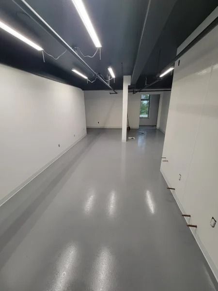Empty, modern room with gray floor, white walls, and black ceiling. Fluorescent lights and a single pillar.