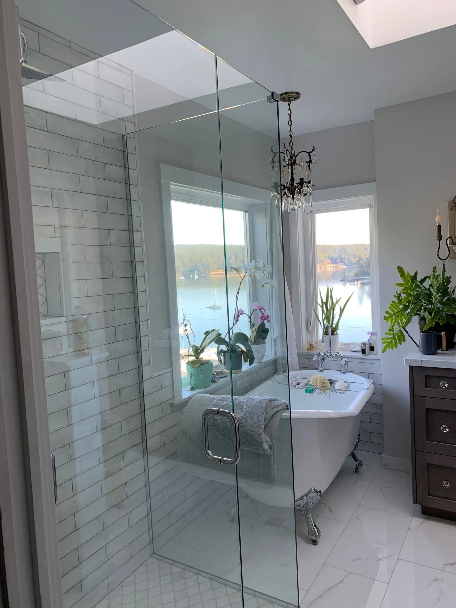 Luxurious bathroom with glass shower, clawfoot tub, water view, and chandelier.