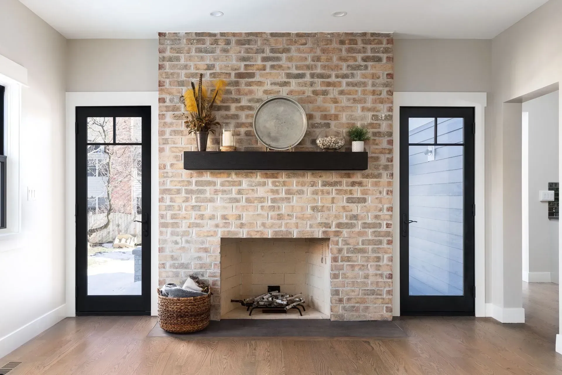 Living room with brick fireplace, black doors, and wood floors.