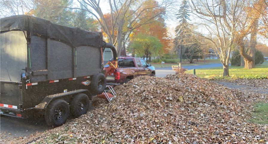 Picture of Ben's Lawn and lanscape performing a leaf removal service. You can see a leaf sucker beening used to clean up a large pile of fallen leaves. 