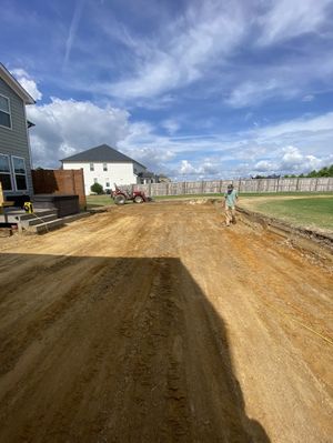 A man is walking down a dirt road in front of a house.