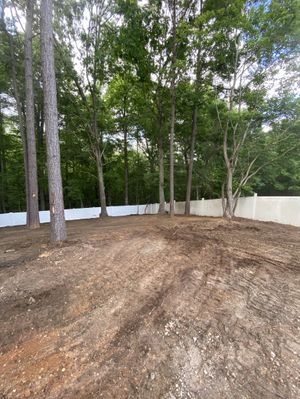 A dirt field with trees in the background and a white fence.