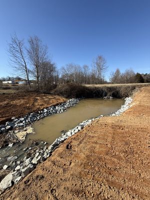 There is a small pond in the middle of a dirt field.