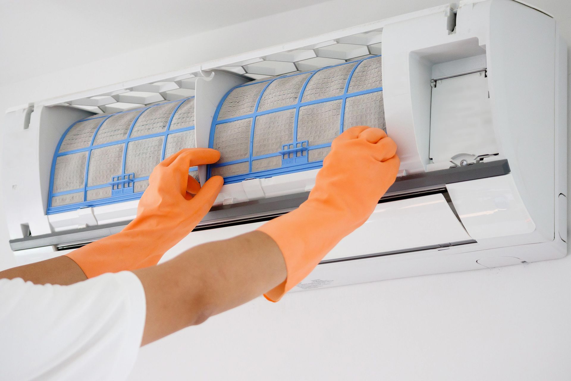 A person wearing orange gloves is cleaning an air conditioner.