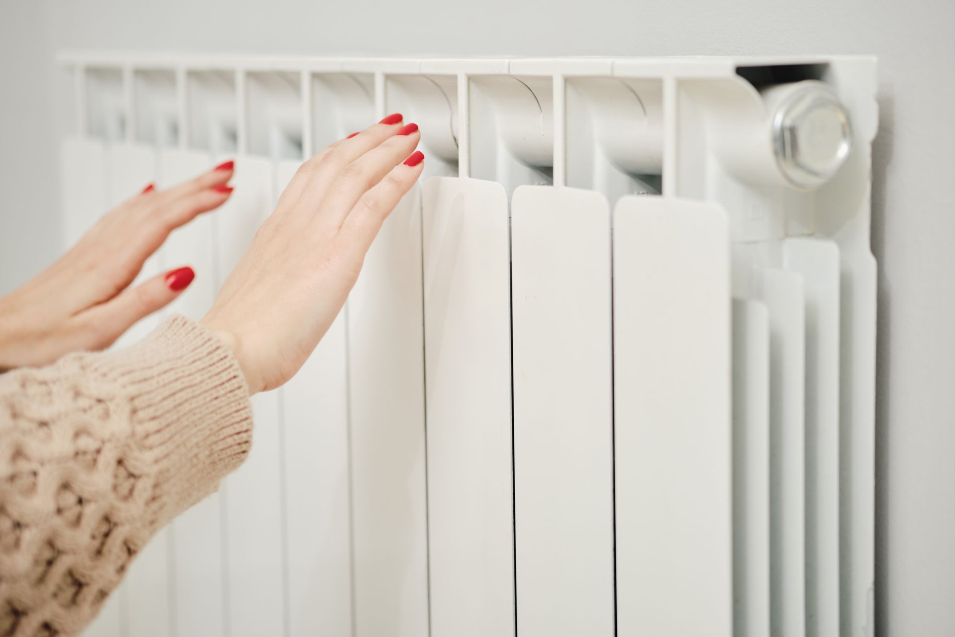 A woman is warming her hands on a radiator.