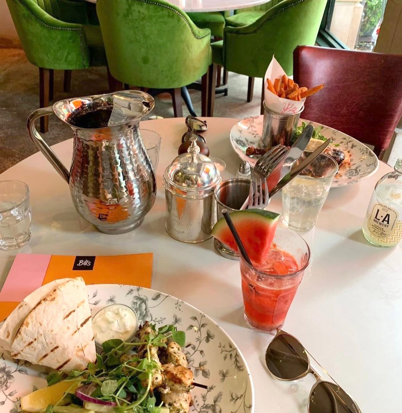 A table set for a meal in a restaurant with food, drinks, silverware, and sunglasses.