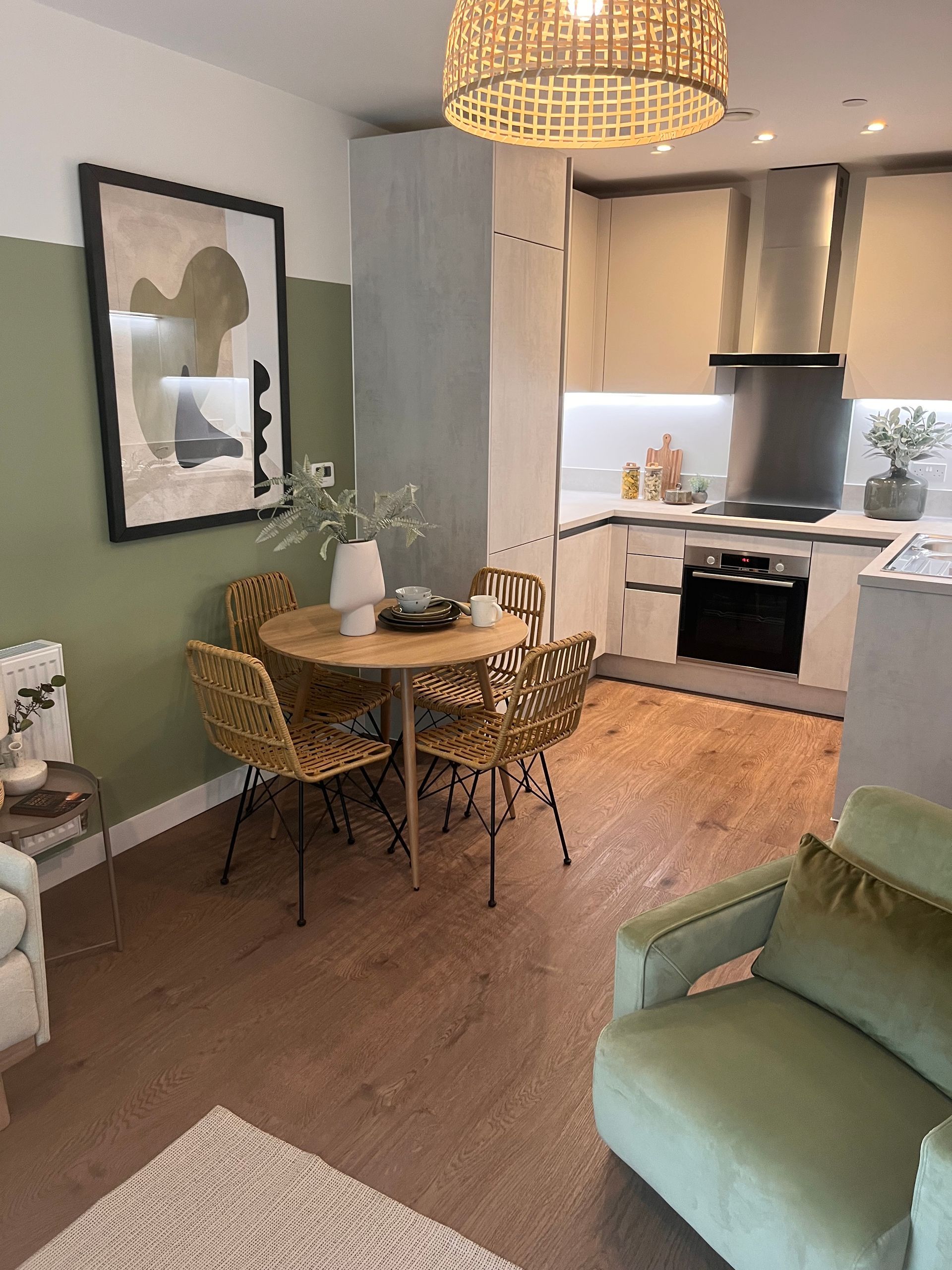 Dining area with round table, rattan chairs, green accents, and an open kitchen.