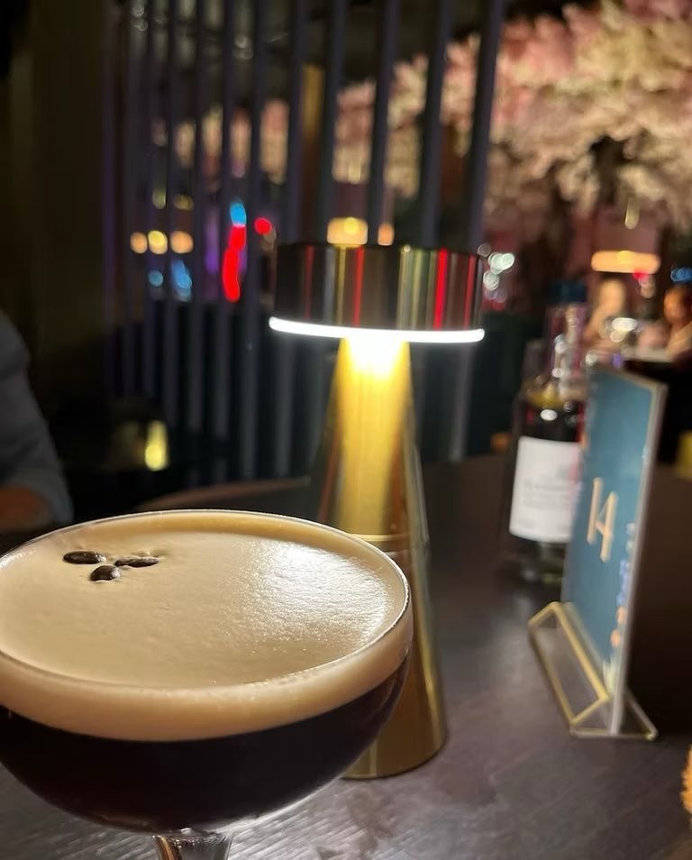 Espresso martini in a glass, with a golden lamp and table number in a dim restaurant setting.