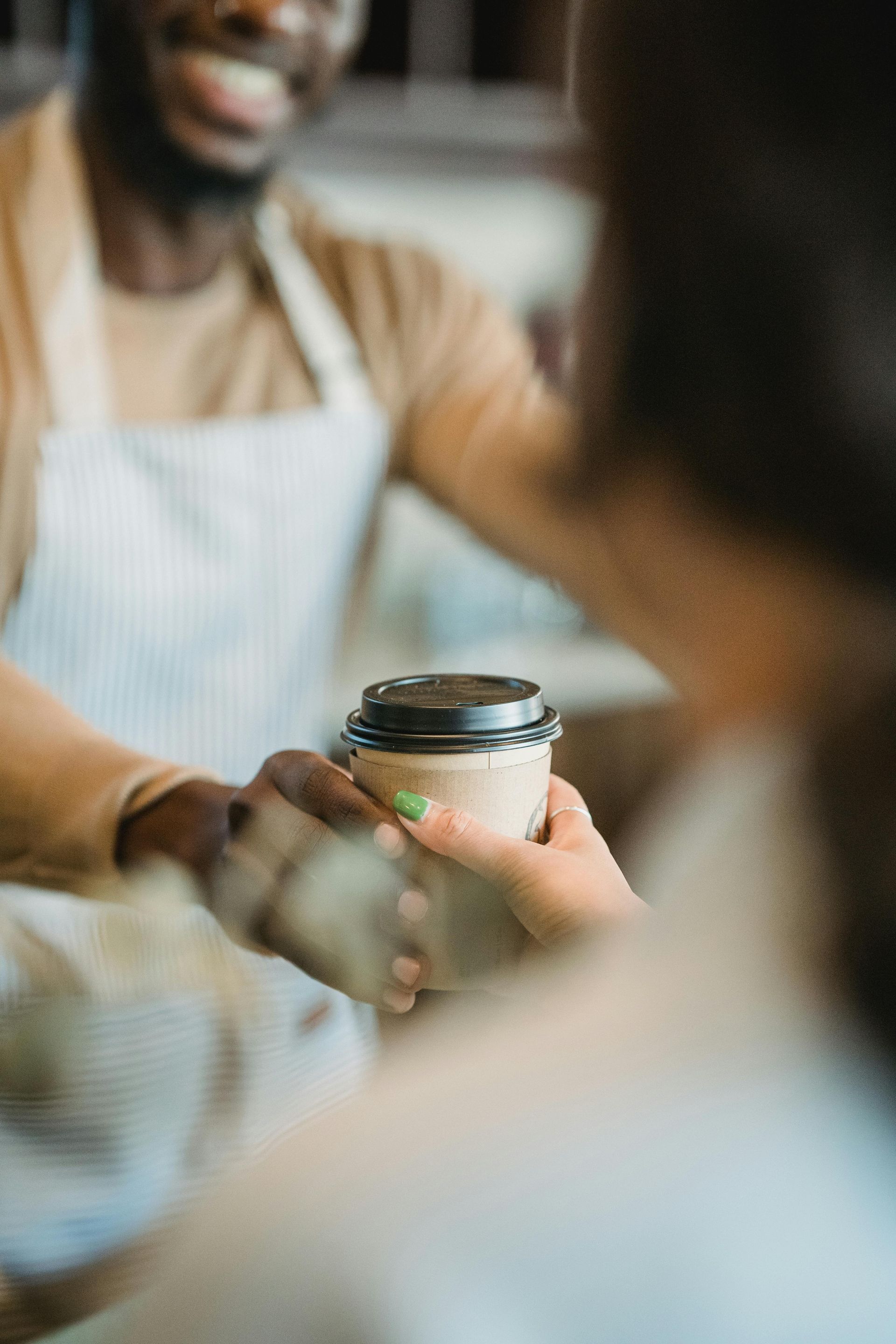 Barista in an apron handing coffee to a customer in a cafe.