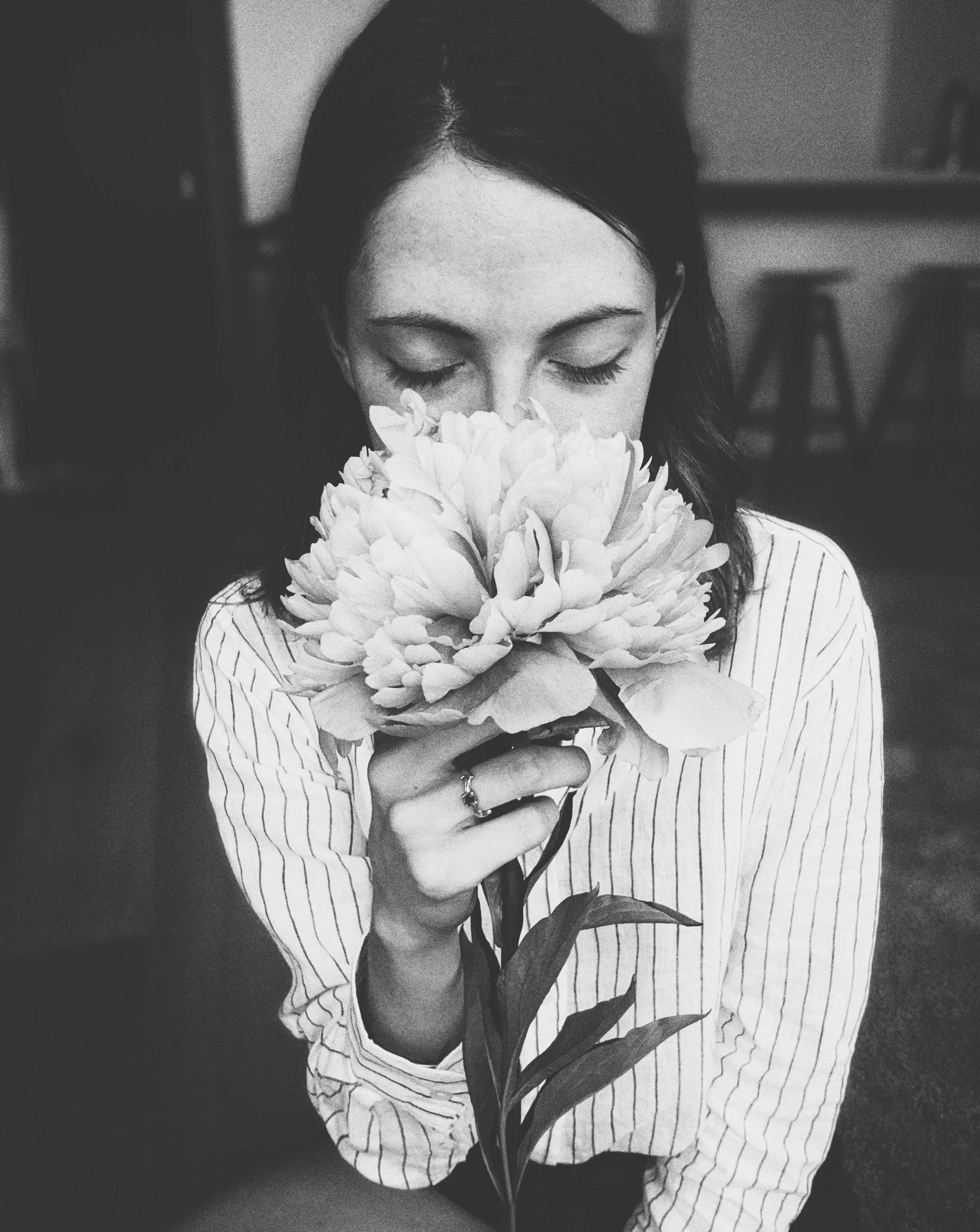 Woman smelling a large, light flower with closed eyes. Black and white, indoors.