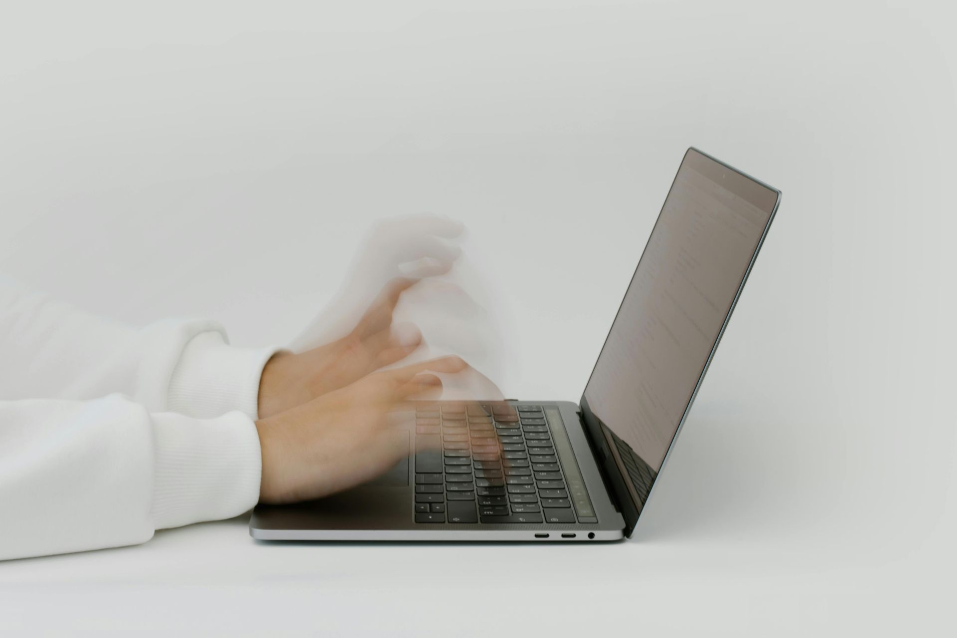 Person's hands typing rapidly on a laptop keyboard against a white backdrop.