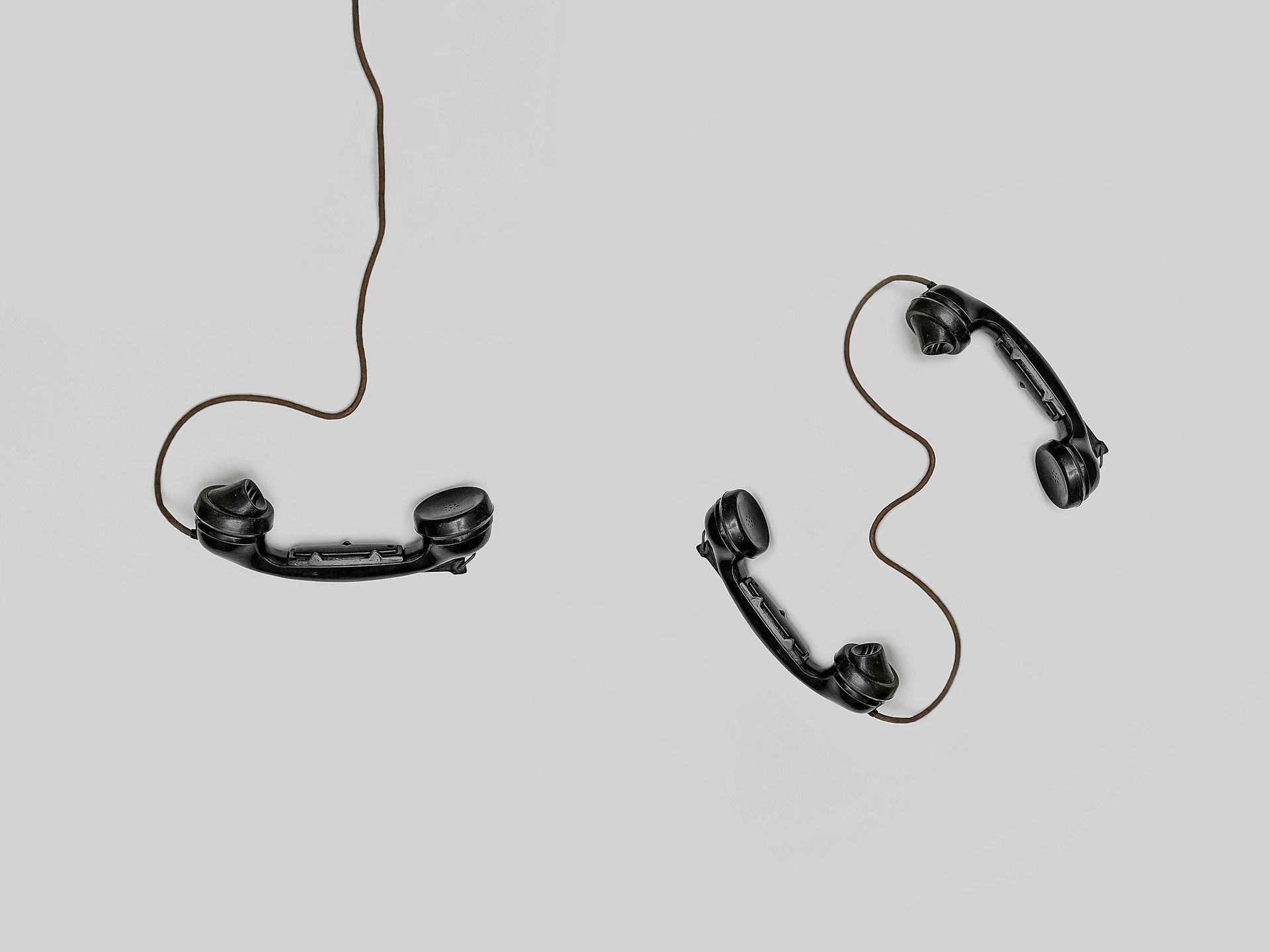 Two vintage black telephone handsets on a gray background, connected by cords.