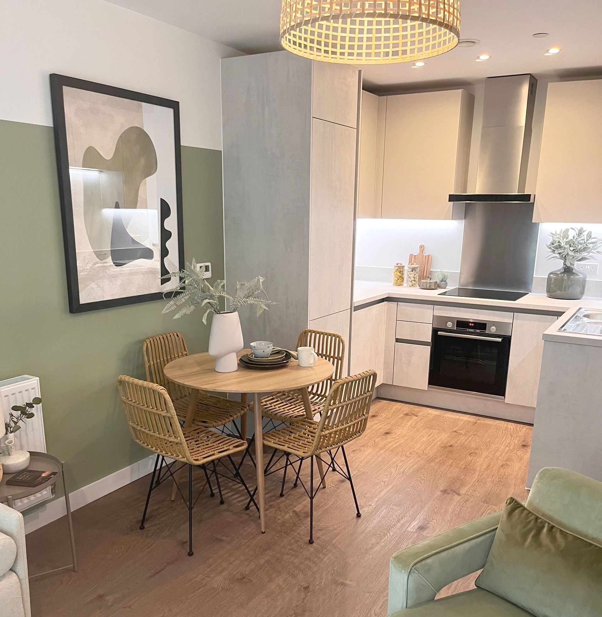 A dining area with a small round table, four wicker chairs, and a kitchen with white cabinets and appliances.