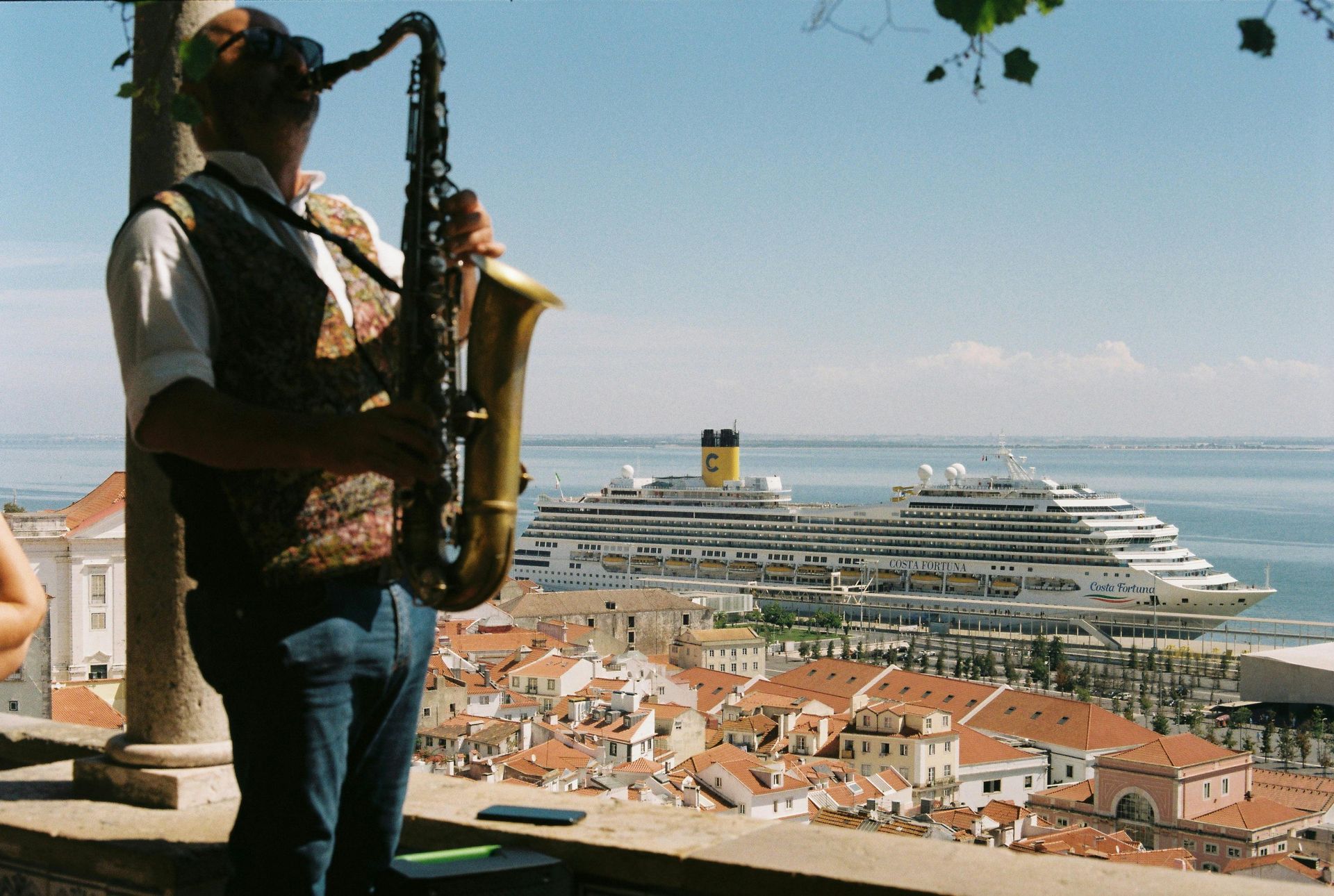 A man playing a saxophone with a cruise ship in the background