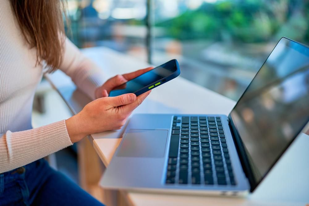 A Woman is Sitting at a Table Using a Laptop and a Cell Phone — River City Communications In Melinga, NSW