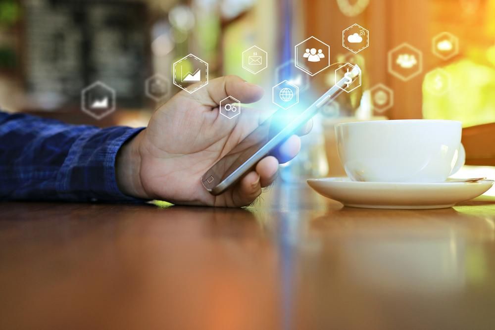 A Person is Using a Smart Phone While Sitting at a Table With a Cup of Coffee — River City Communications In Wingham, NSW