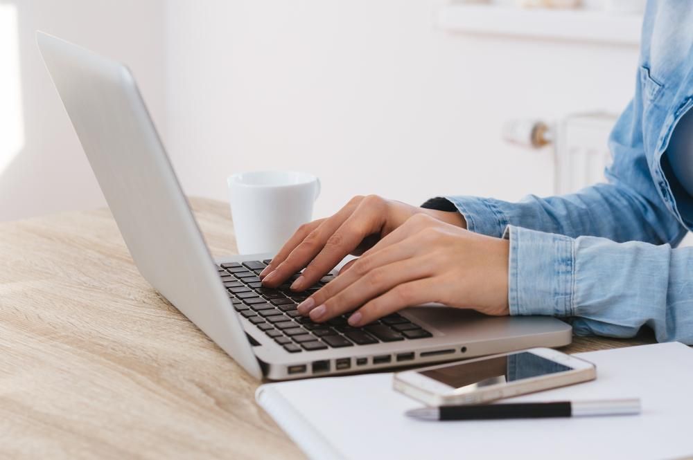 A Woman is Typing on a Laptop Computer While Sitting at a Desk — River City Communications In Forster, NSW